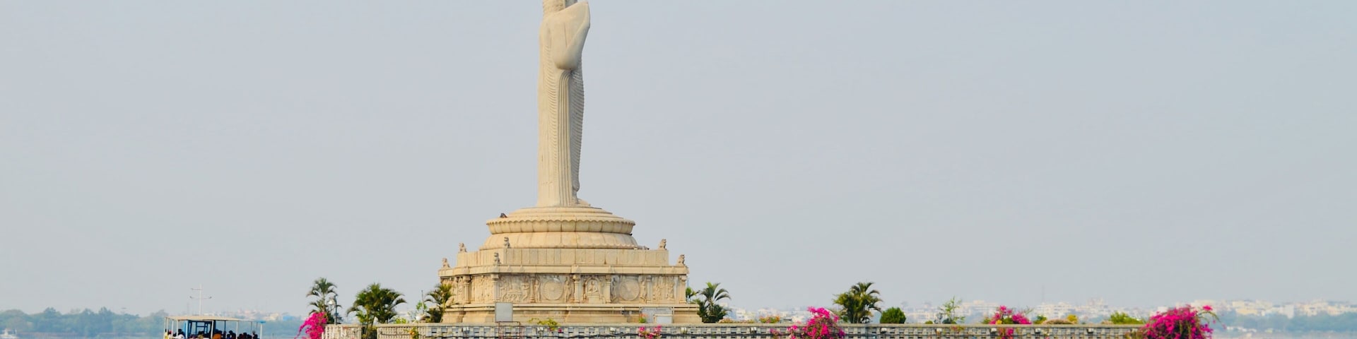 Un monumento alto con una estatua en la parte superior, rodeado de agua y un muelle con un bote.