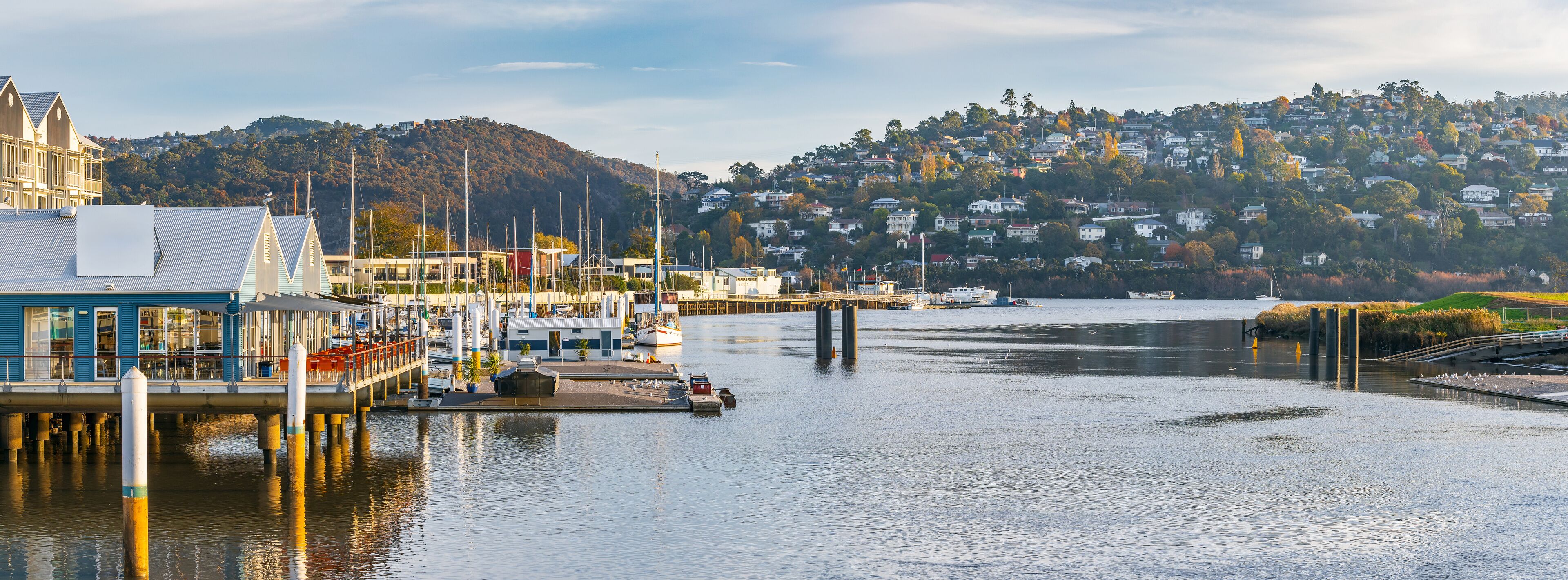 Panorama view of buildings and jetties along a riverside marina with houses on distant a hillside