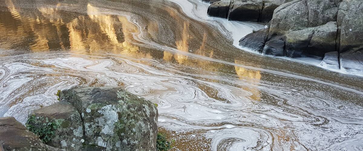 A natural rock formation with a reflective water body and a large boulder in the foreground.