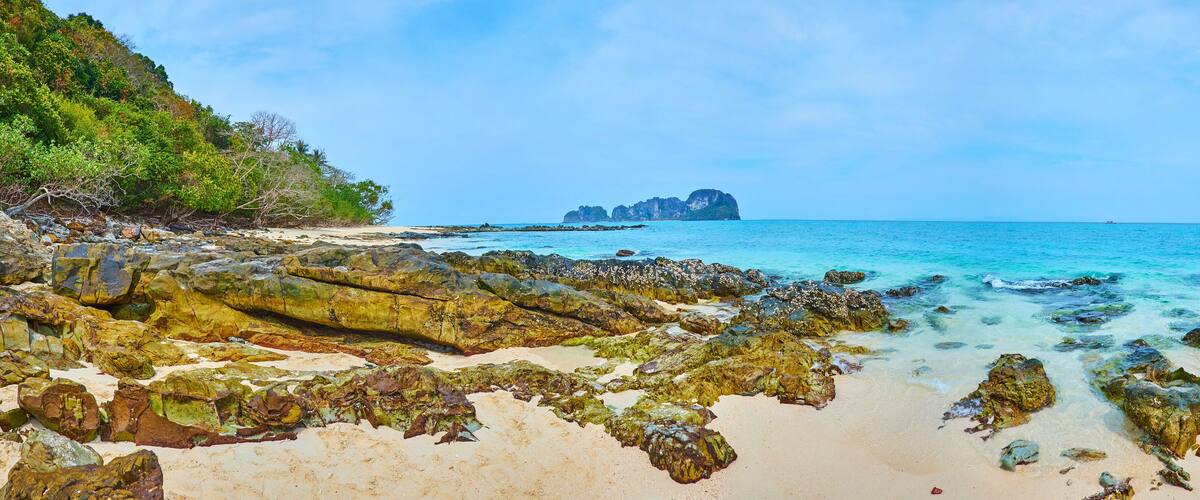 A rocky beach with clear turquoise water and a distant island.