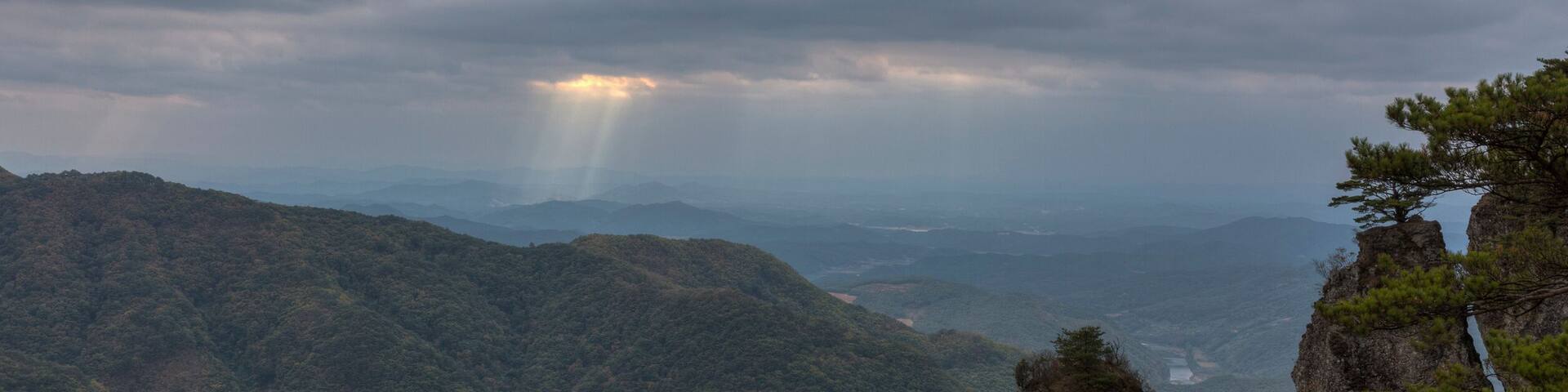 Un paisaje montañoso con un afloramiento rocoso destacado y un pino.