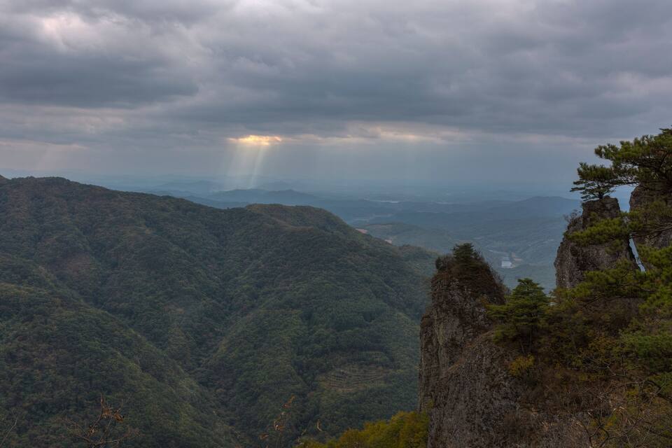 Un paisaje montañoso con un afloramiento rocoso destacado y un pino.