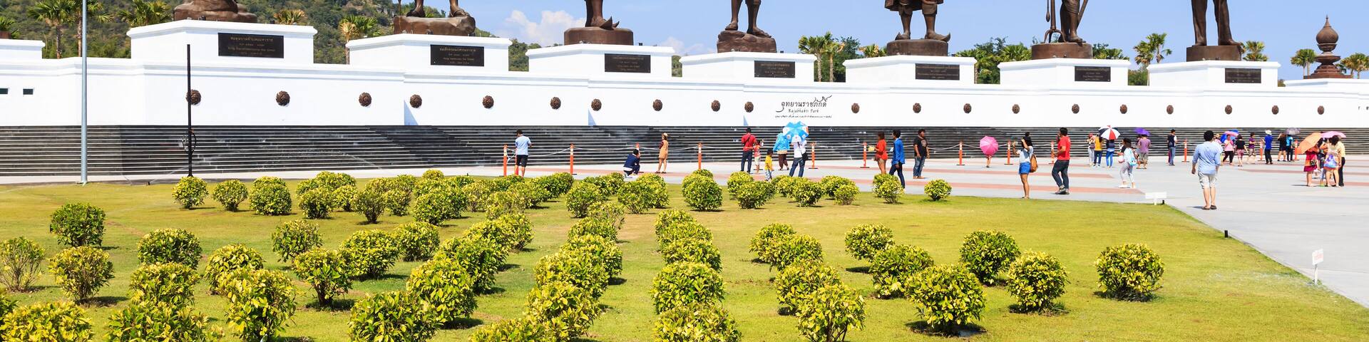A row of bronze statues on pedestals, a white building with a sign, and a well-maintained grassy area with bushes.