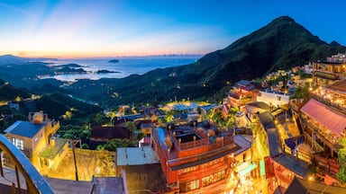 Un pueblo costero al anochecer, con edificios iluminados, una montaña destacada y vista al mar.