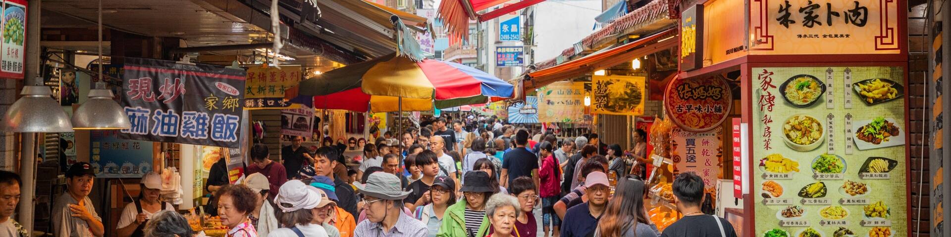 A crowded street market with various food stalls and people shopping.
