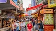 Un marché de rue animé, avec de nombreux étals de nourriture et des gens qui font leurs courses.