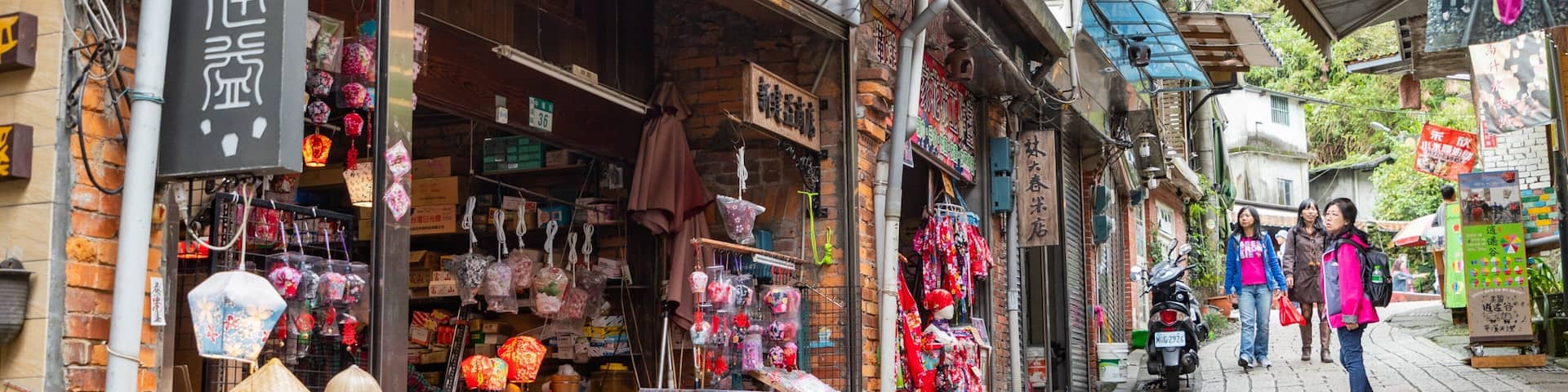 A narrow street with shops selling lanterns, textiles, and other goods.