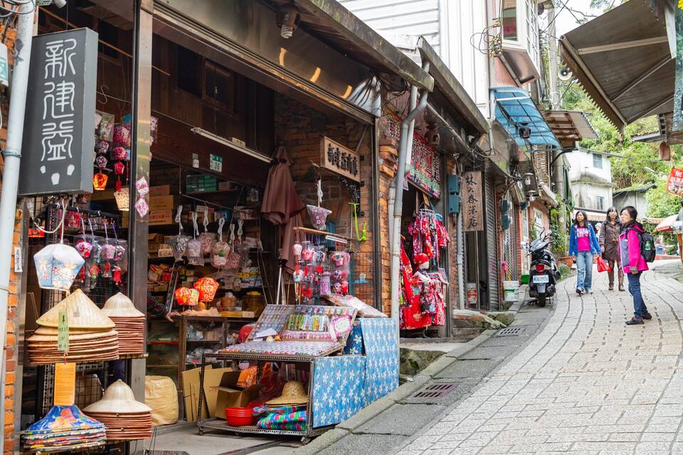 A narrow street with shops selling lanterns, textiles, and other goods.