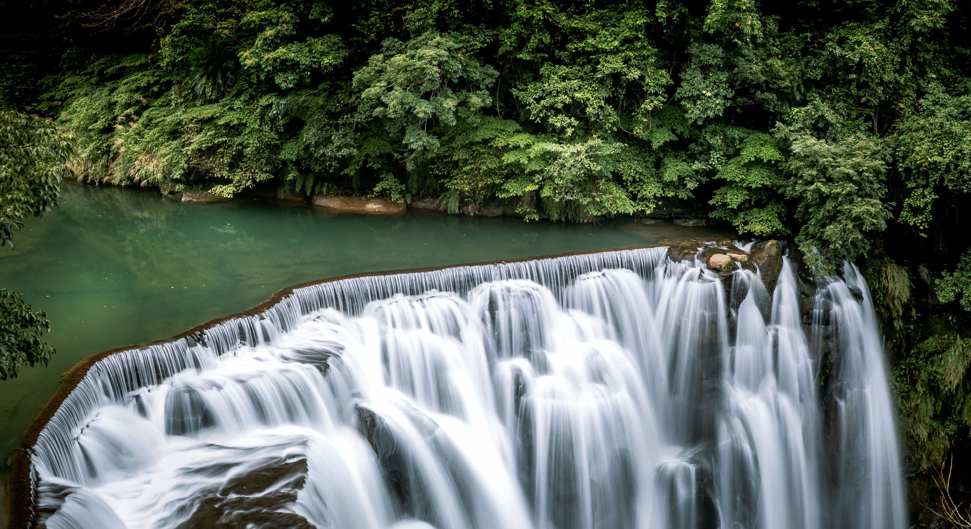 Uma cascata despenca em um rio, cercado por floresta densa.