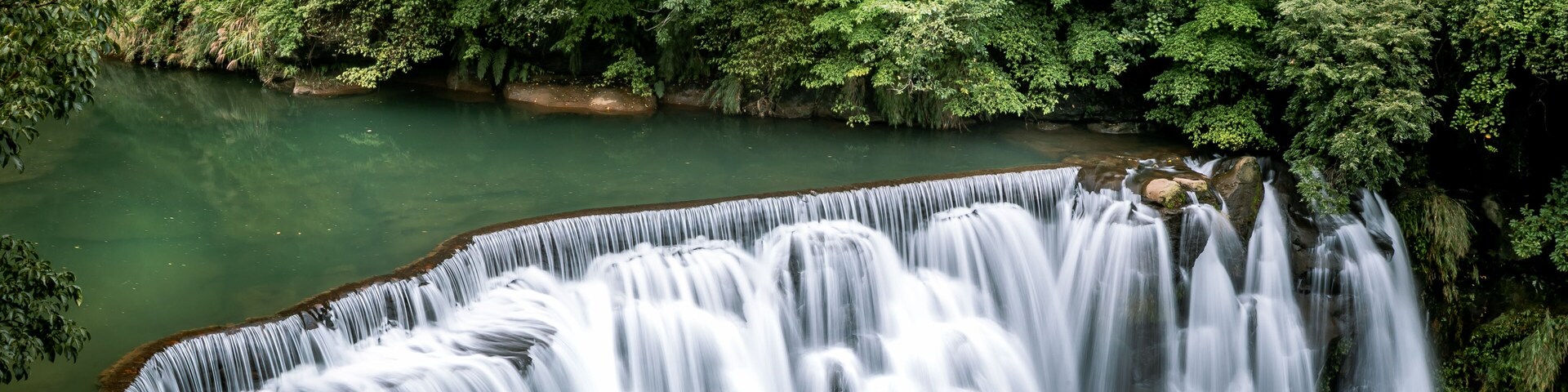 Uma cascata despenca em um rio, cercado por floresta densa.