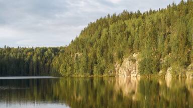 Une jetée en bois s’étendant sur des eaux calmes, avec une colline boisée en arrière-plan.