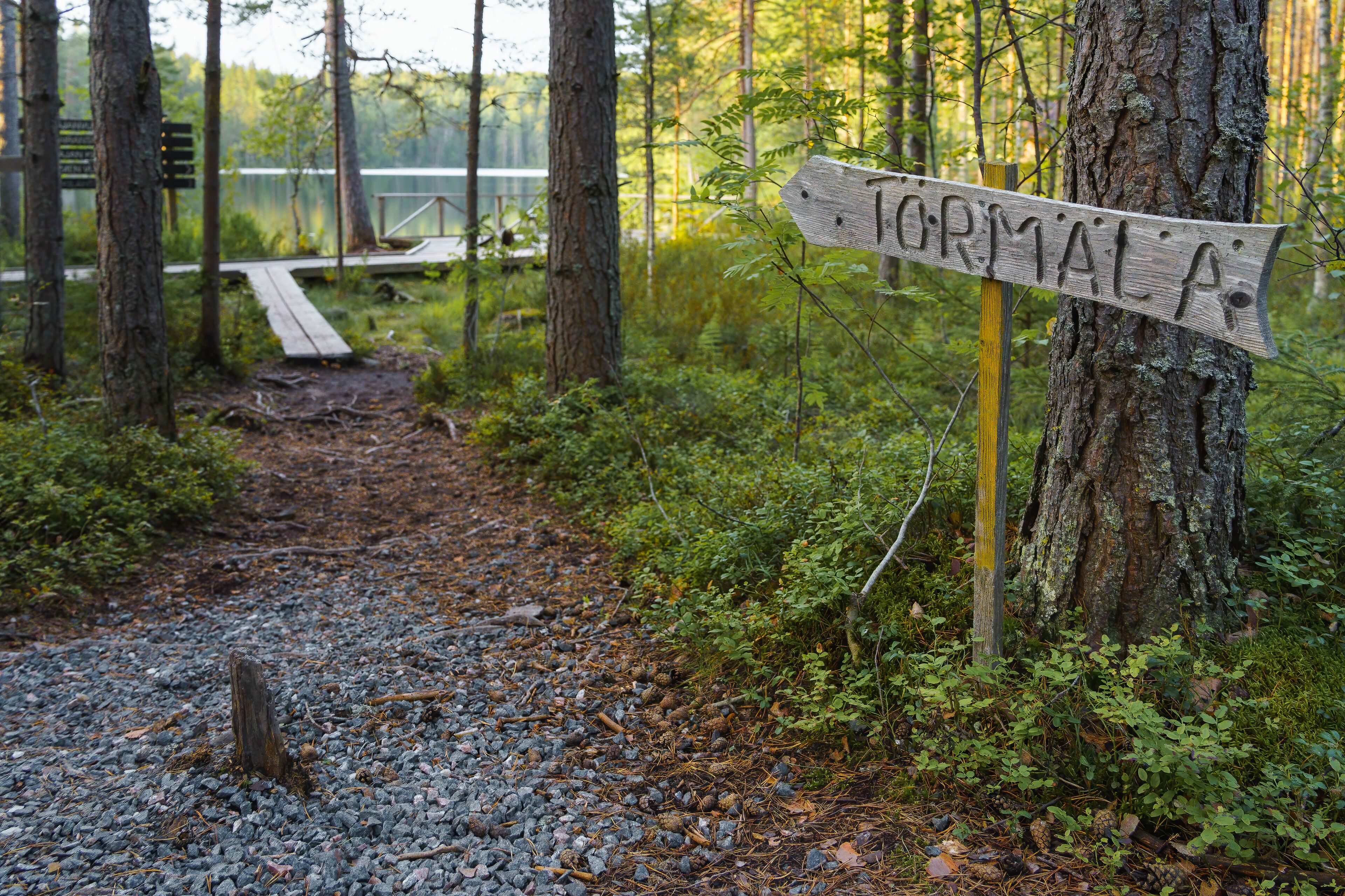 A forested area with a gravel path leading to a wooden sign that reads "FORMALA."