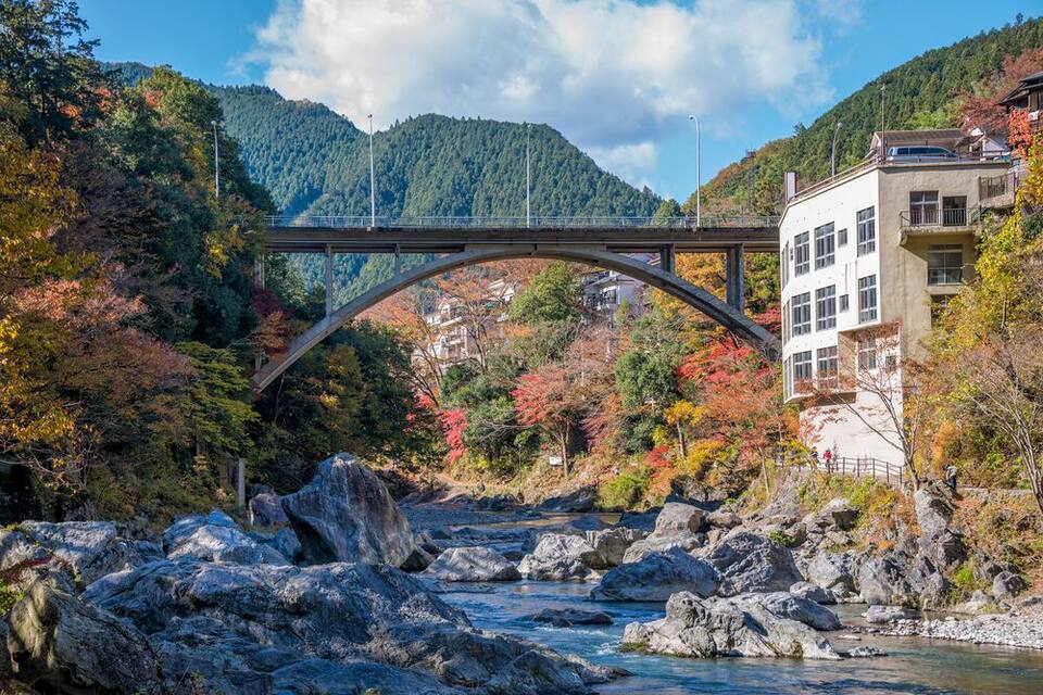 A stone bridge over a river, surrounded by autumn foliage and mountains.