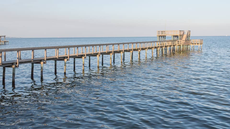 Fishing piers stretching out over Galveston Bay in Kemah, Texas, USA. Foot pier for saltwater fishing of vacation home/beach house rental/bay home in Lighthouse District waterfront at sunset. Panorama