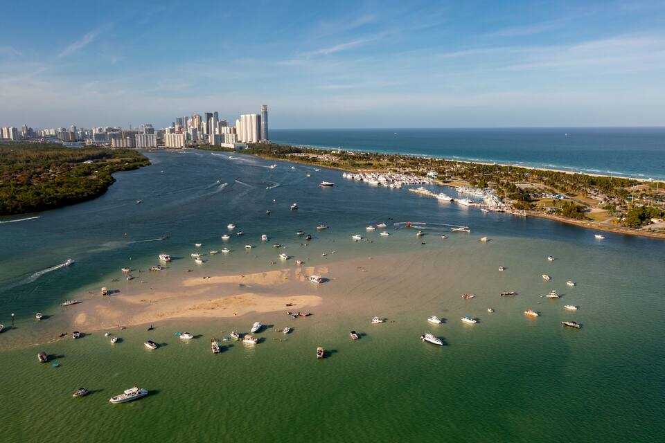Vista aérea de una ciudad costera con un puerto deportivo, barcos y el horizonte urbano.