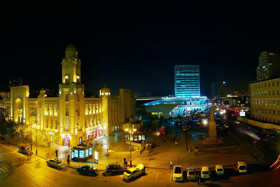 A historic building with a large dome and clock tower, surrounded by modern buildings and busy streets at night.