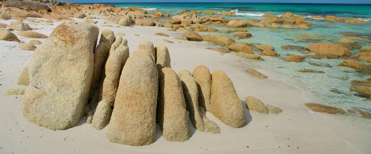 A beach with large boulders and clear turquoise water.