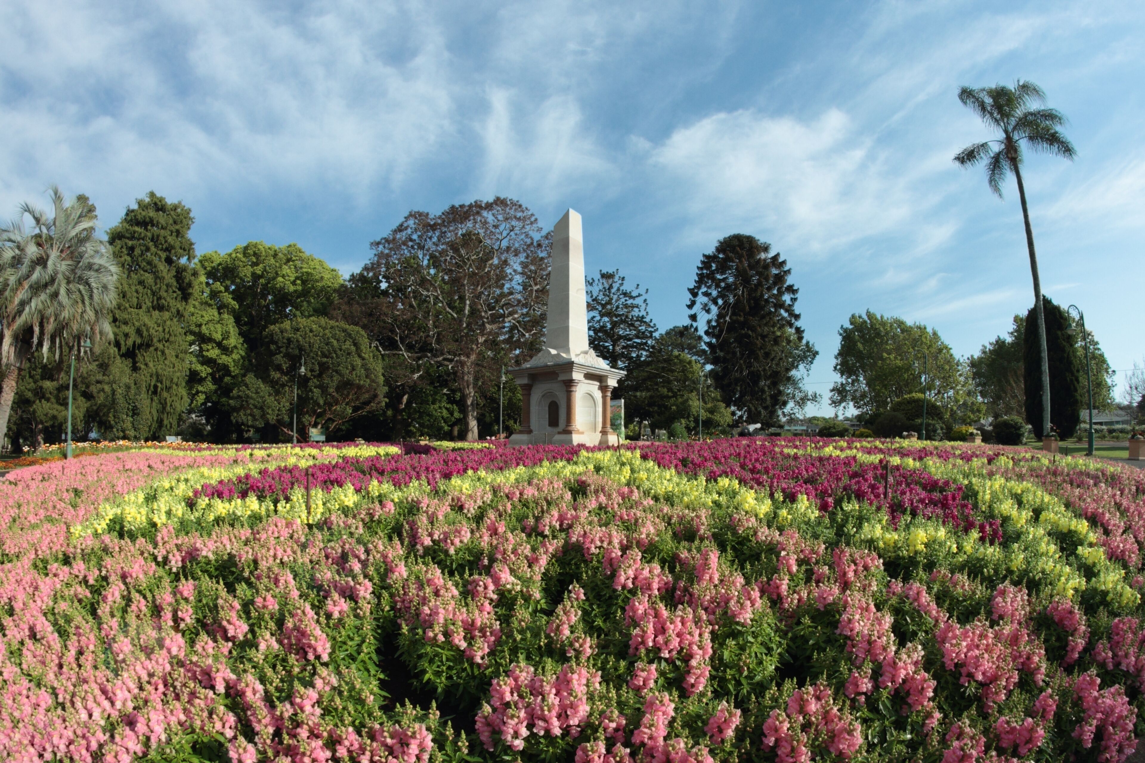 A monument surrounded by a circular flower garden with pink and yellow flowers.