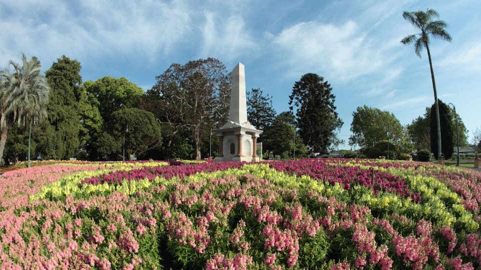 A monument surrounded by a circular flower garden with pink and yellow flowers.