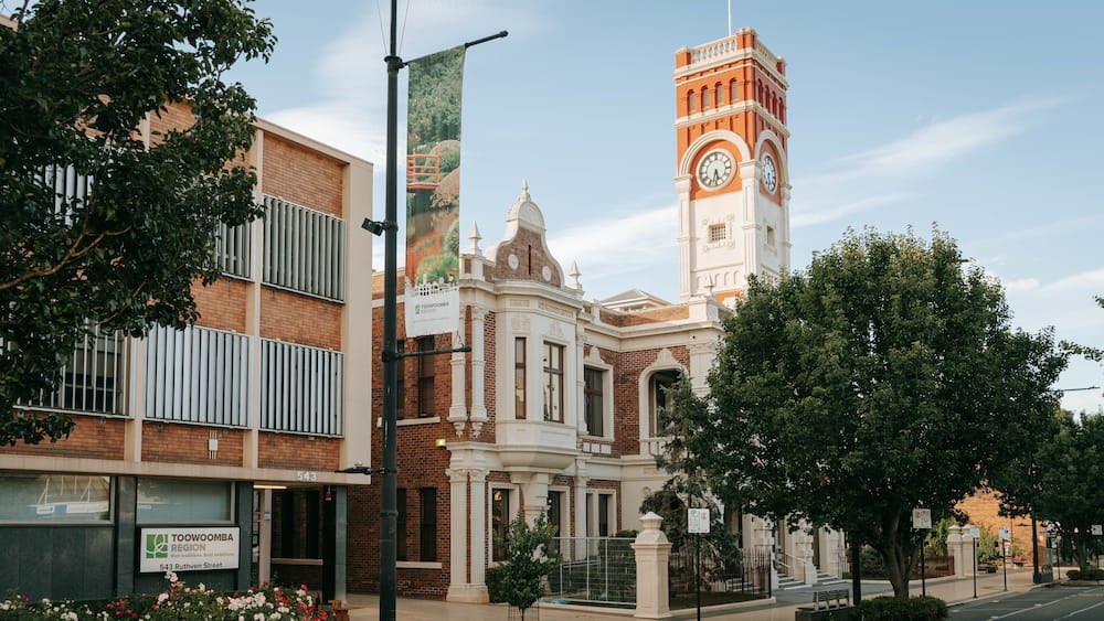 A historic building with a clock tower, surrounded by trees and modern buildings.