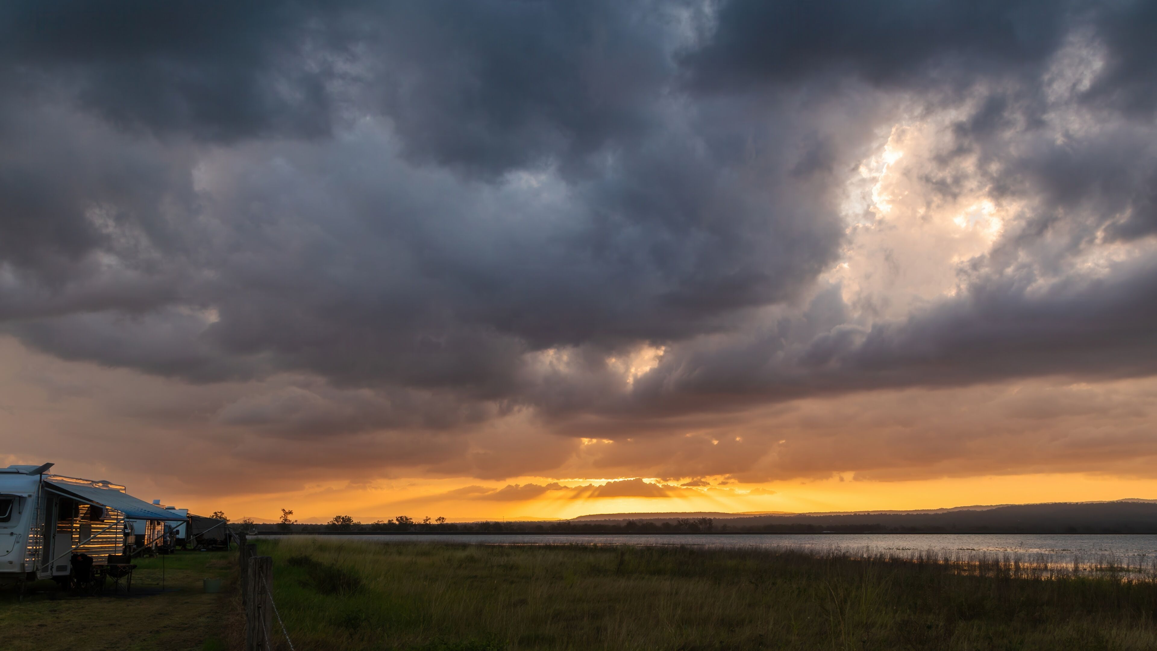 A cloudy sky over a grassy field with a trailer and a body of water in the distance.