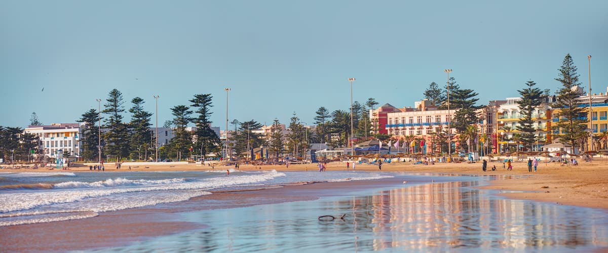 A beach with waves, people, and colorful buildings in the background.