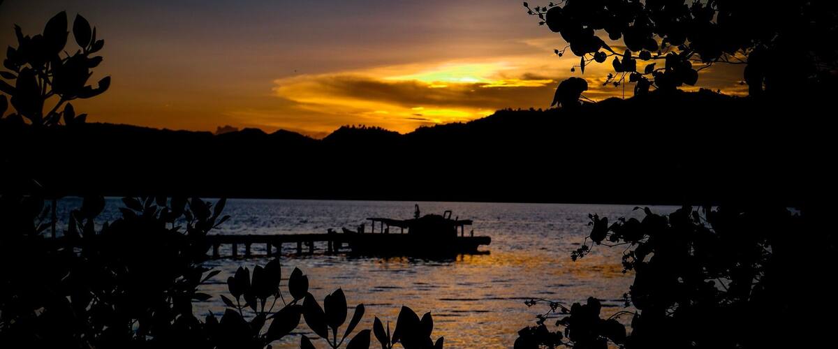 A sunset over a body of water with a boat on a pier.
