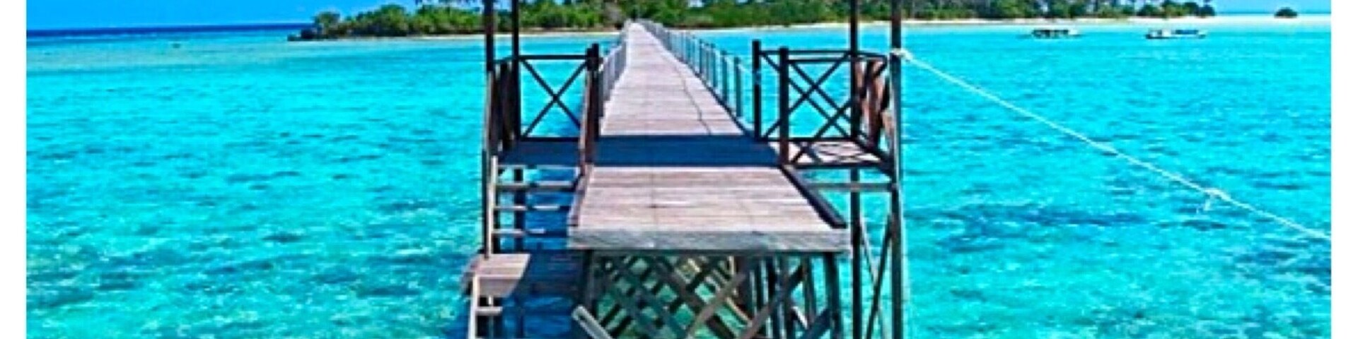 A wooden pier leading to a thatched-roof structure over turquoise waters.