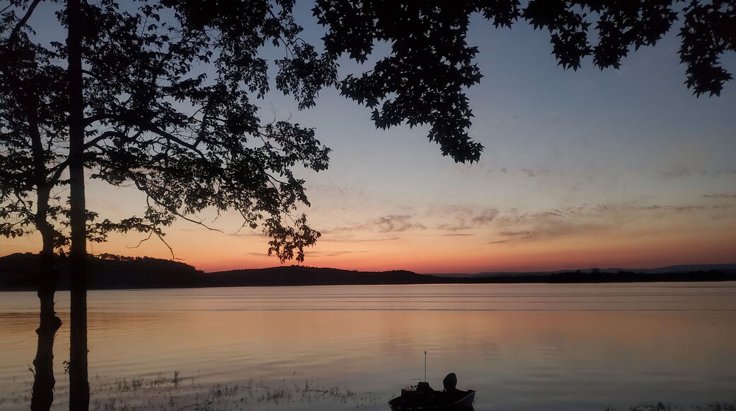 Silhouetted boat on a calm lake at sunset with trees in the foreground