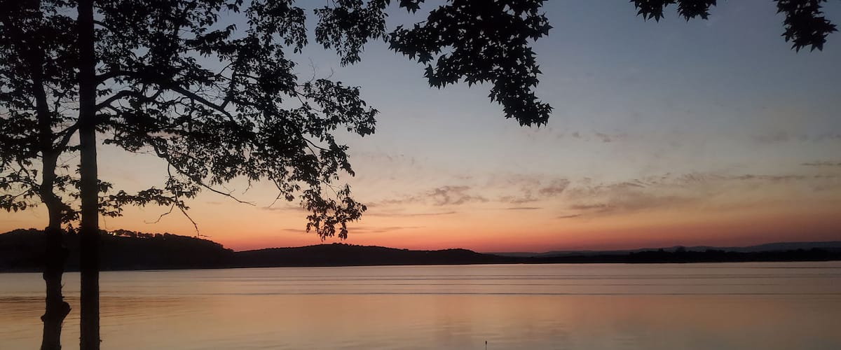 Silhouetted boat on a calm lake at sunset with trees in the foreground