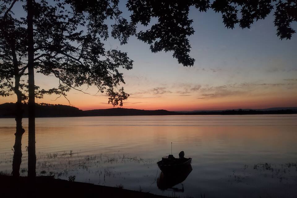 Um barco num lago calmo ao pôr do sol, com árvores recortadas contra o céu.