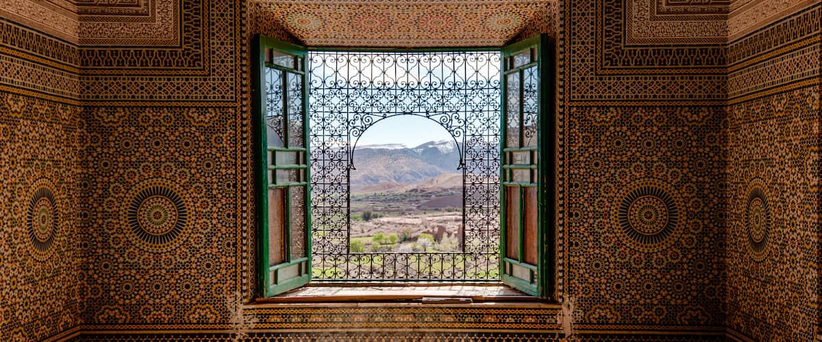Una habitación ornamentada con detalles de azulejos intrincados y vistas a un paisaje montañoso a través de un vano abierto.