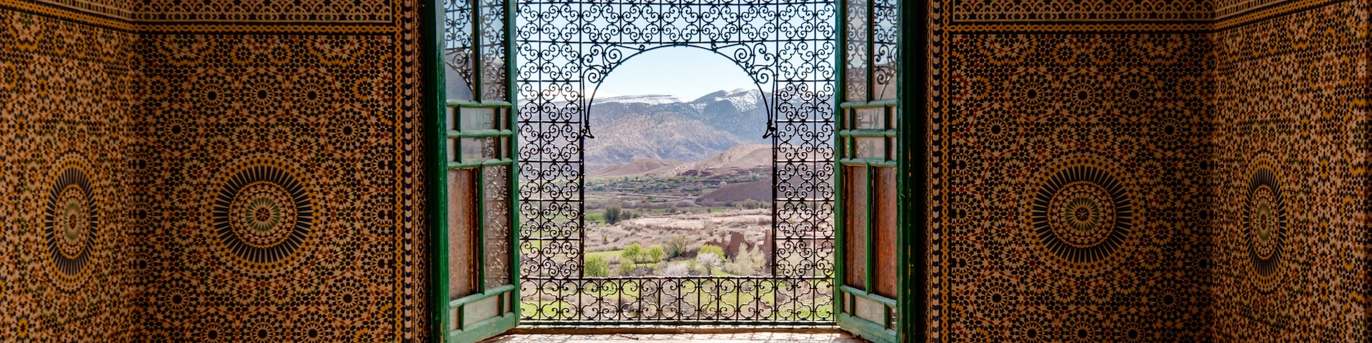 Una habitación ornamentada con detalles de azulejos intrincados y vistas a un paisaje montañoso a través de un vano abierto.