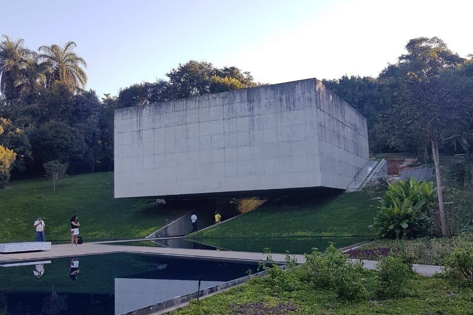 A modern concrete structure with a sloped roof, surrounded by a grassy area and a small pond.