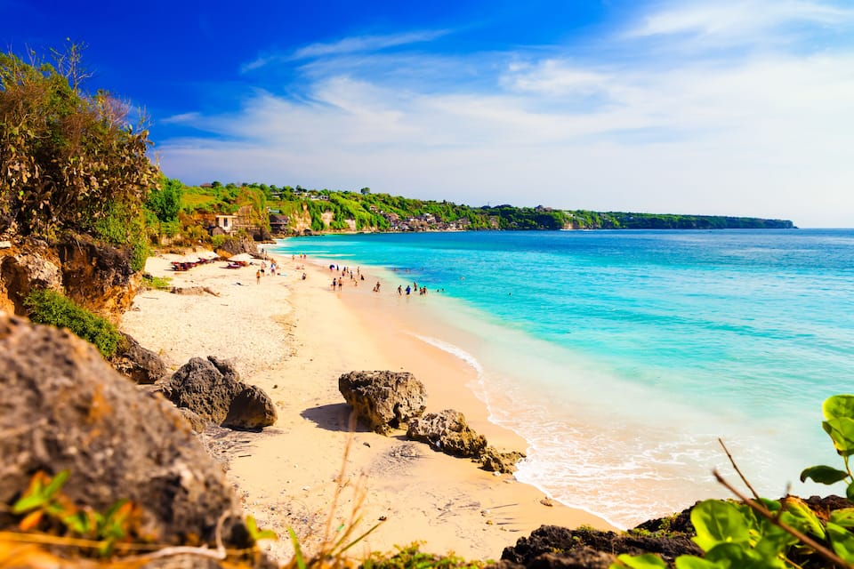 A beach with clear turquoise waters, sandy shore, and rocky outcrops.