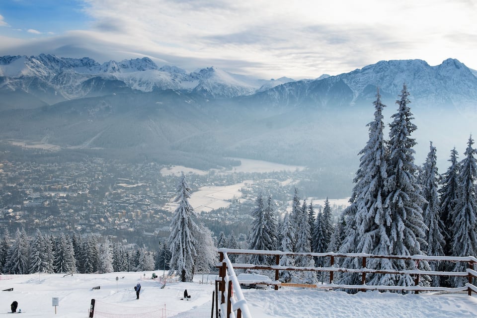 Un paysage montagneux enneigé avec une station de ski, des arbres recouverts de neige et des montagnes lointaines.