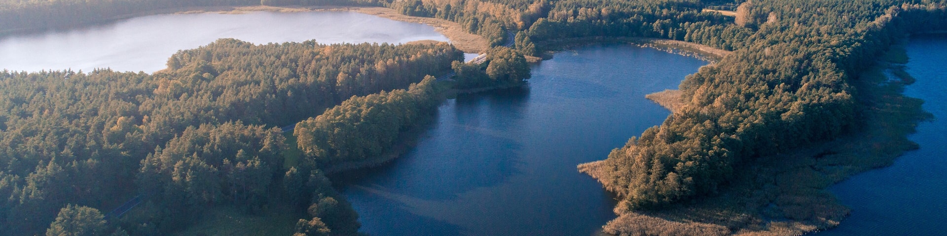 Une vue aérienne d’une rivière qui serpente à travers une zone densément boisée, avec une petite île et un pont.