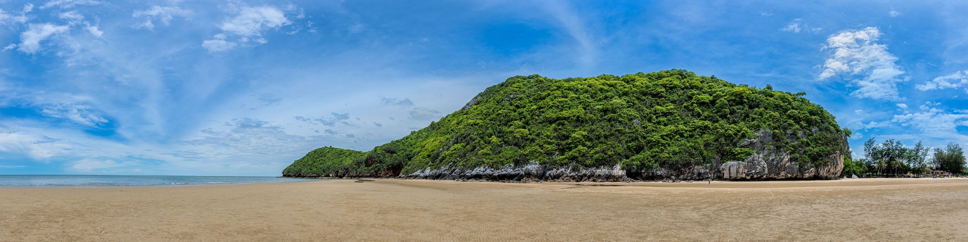 A beach with a large green hill in the background.
