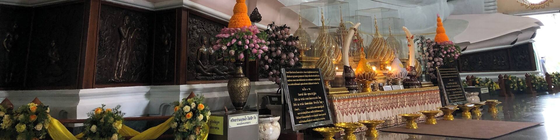 A large white reclining Buddha statue in a temple interior with ornate decorations and floral arrangements.