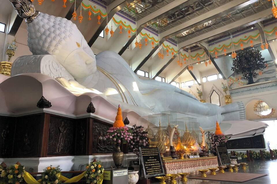 A large white reclining Buddha statue in a temple interior with ornate decorations and floral arrangements.