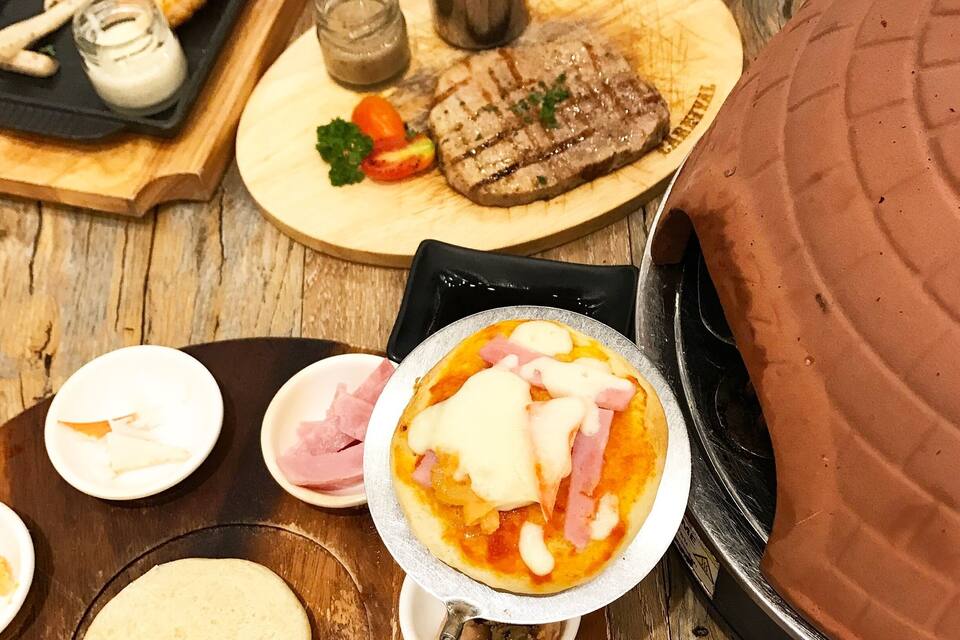 Diversos pratos, incluindo bife grelhado, espiga de milho e pizza com fiambre e queijo.