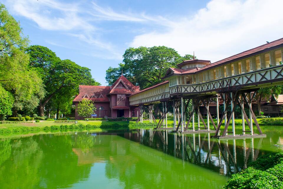 A traditional building with a red roof, a bridge over a pond, and lush greenery.