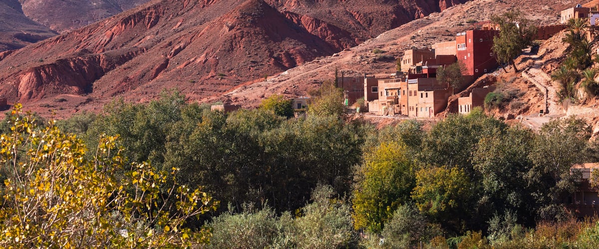 A rugged mountainous landscape with reddish terrain and a small settlement with traditional buildings.
