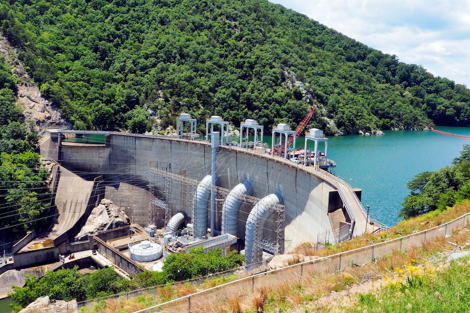 A hydroelectric dam with multiple turbines, surrounded by lush greenery and a calm lake.