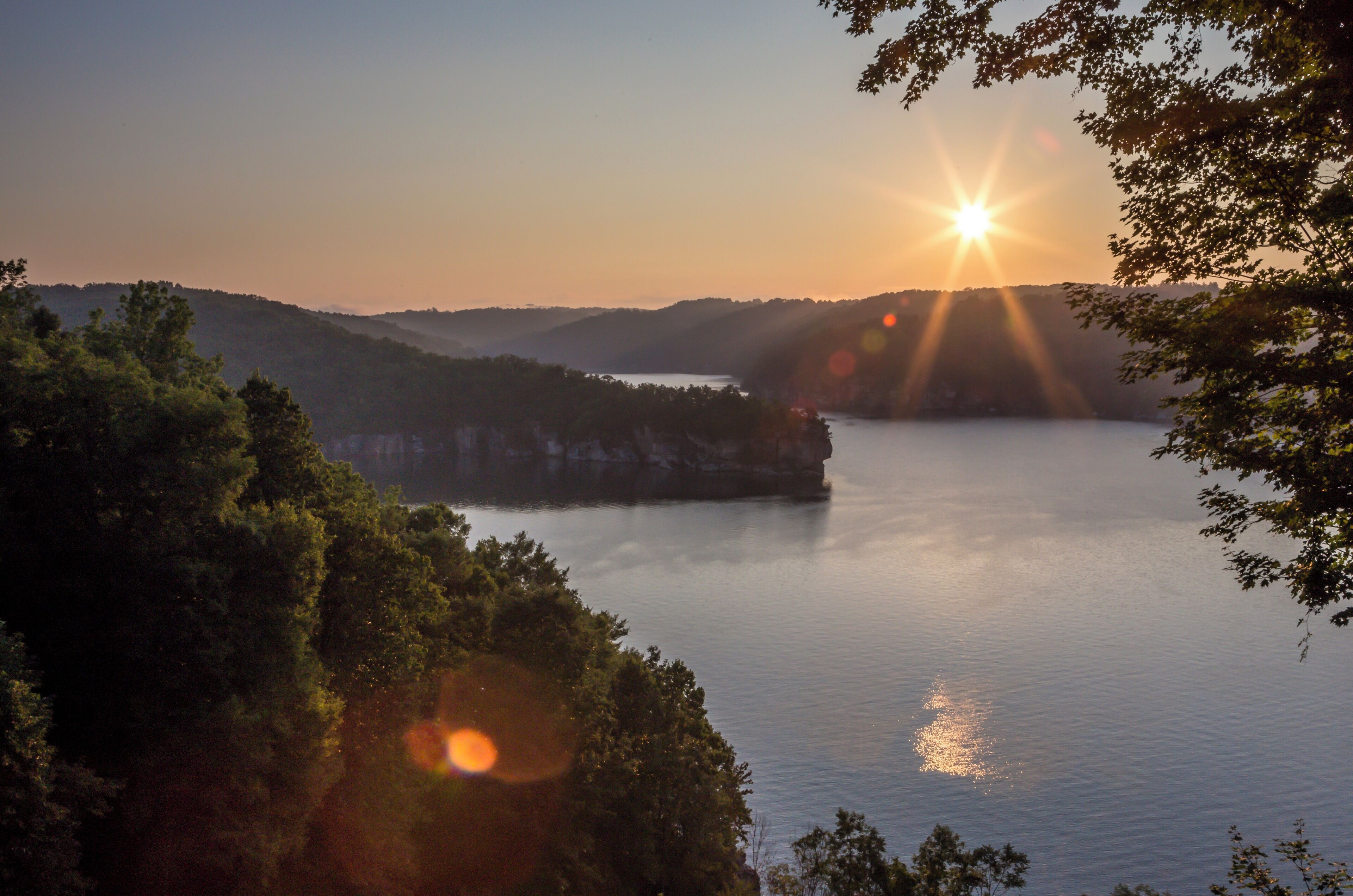 A sunset over a calm lake with surrounding hills and trees.