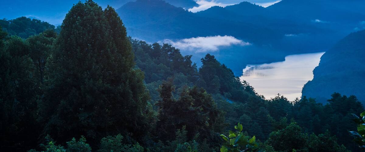 A mountainous landscape with a valley and a lake at sunrise.