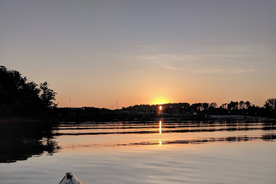 A kayak on calm water with a sunset in the background.