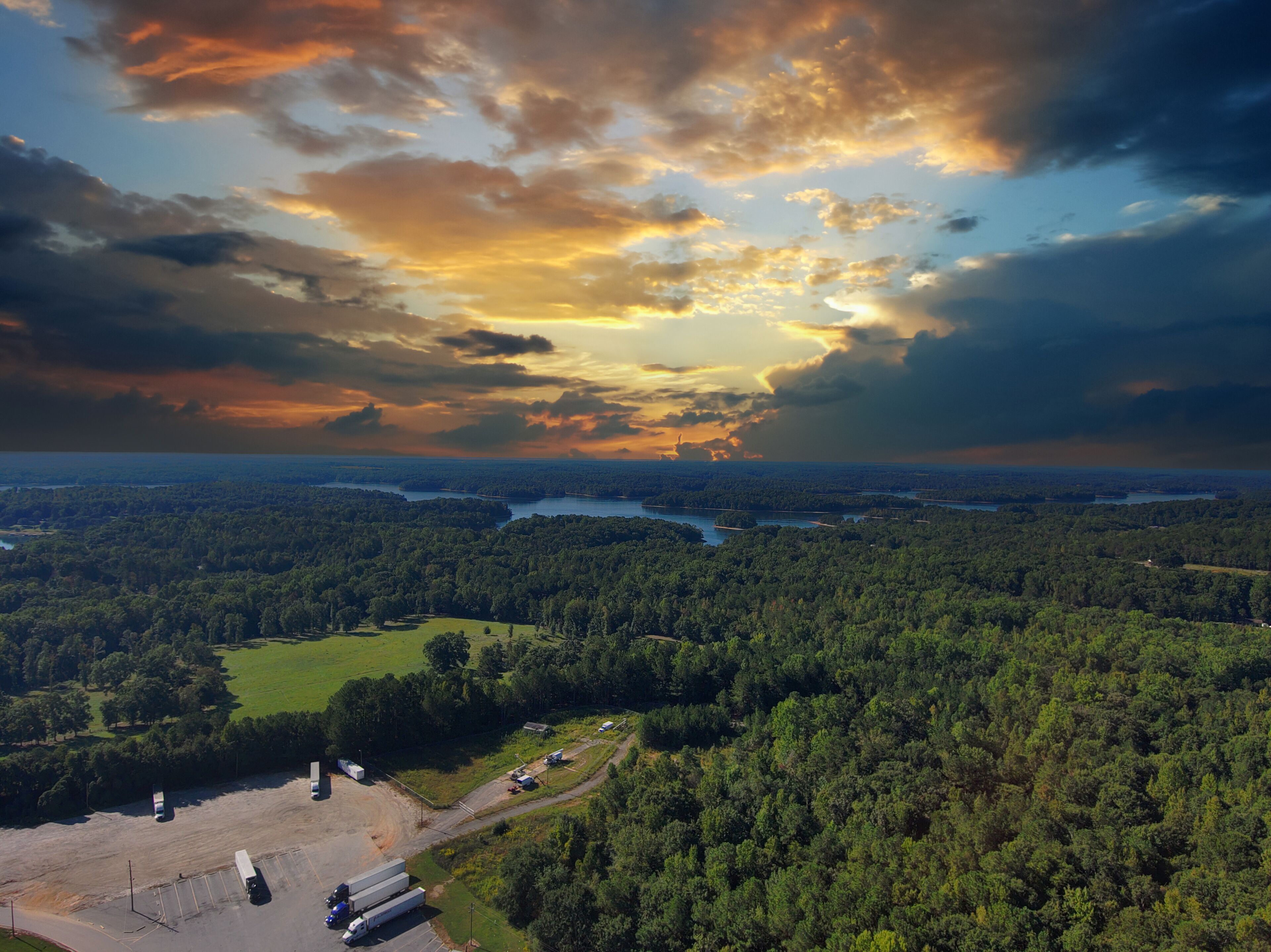 a stunning aerial shot of the blue waters of Lake Hartwell surrounded by vast miles of lush green trees and grass with powerful clouds at sunset in Fair Play South Carolina USA