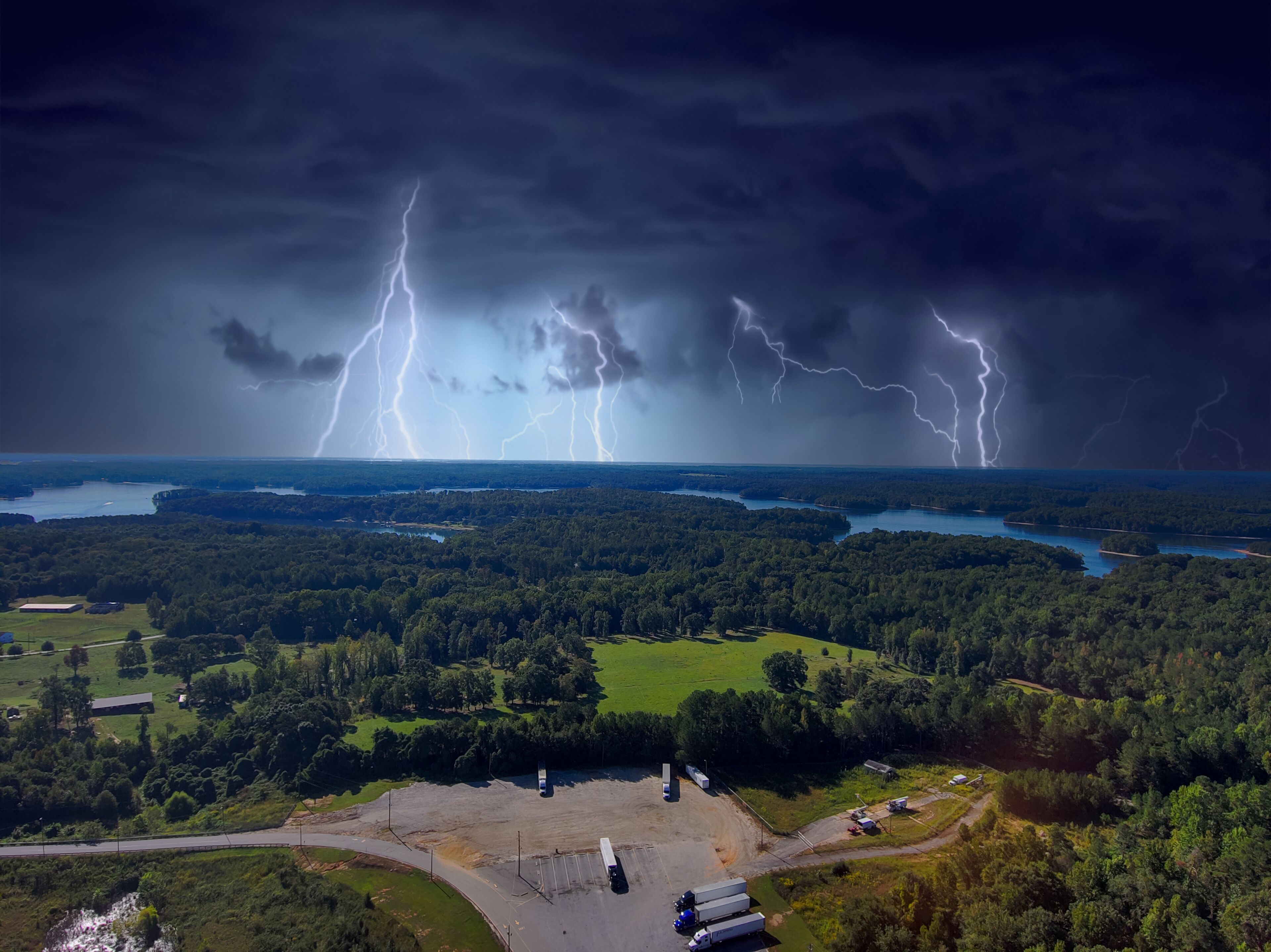 a stunning aerial shot of the blue waters of Lake Hartwell surrounded by vast miles of lush green trees and grass with powerful storm clouds and lightning in Fair Play South Carolina USA