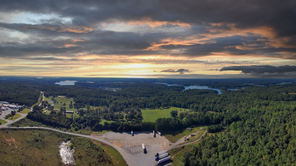 An aerial view of a forested landscape with a river, a parking lot, and a bridge.